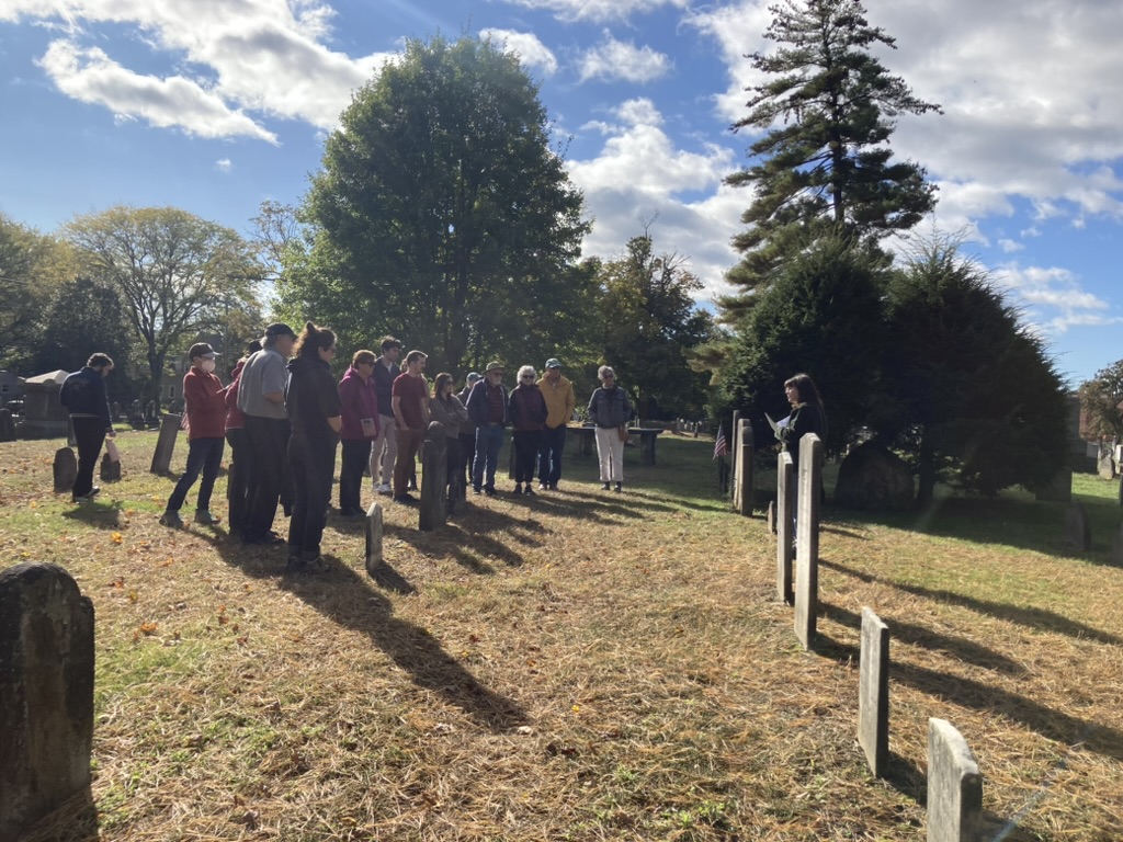 A person talks to a small crowd in a cemetery.